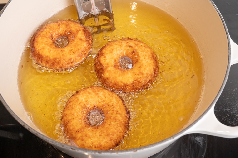 Oponki donuts are being fried in a large pot filled with oil.
