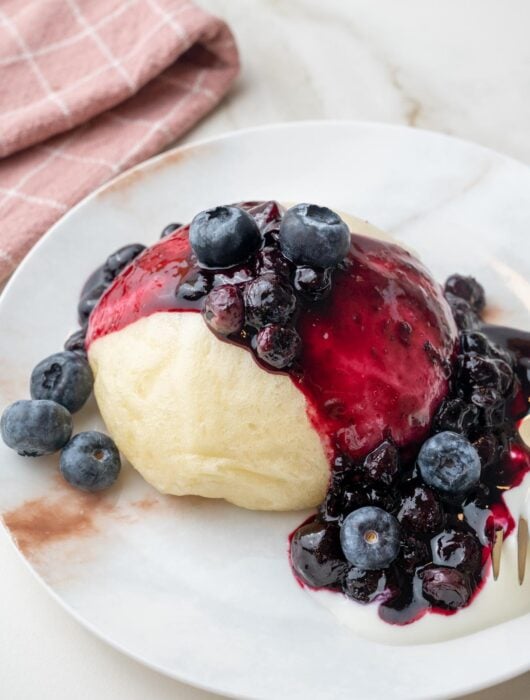 Steamed bun with blueberry sauce and yogurt on a white plate.