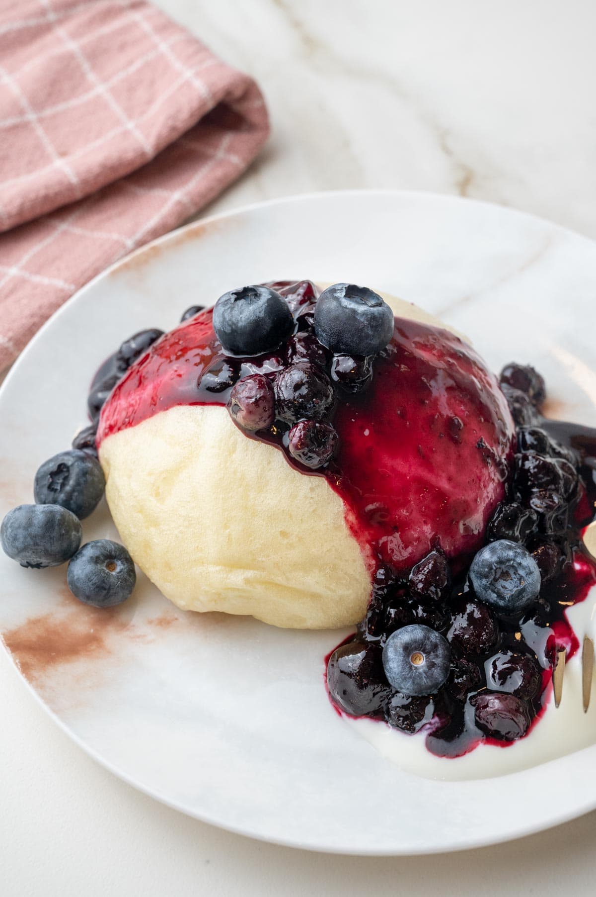 Steamed bun with blueberry sauce and yogurt on a white plate.