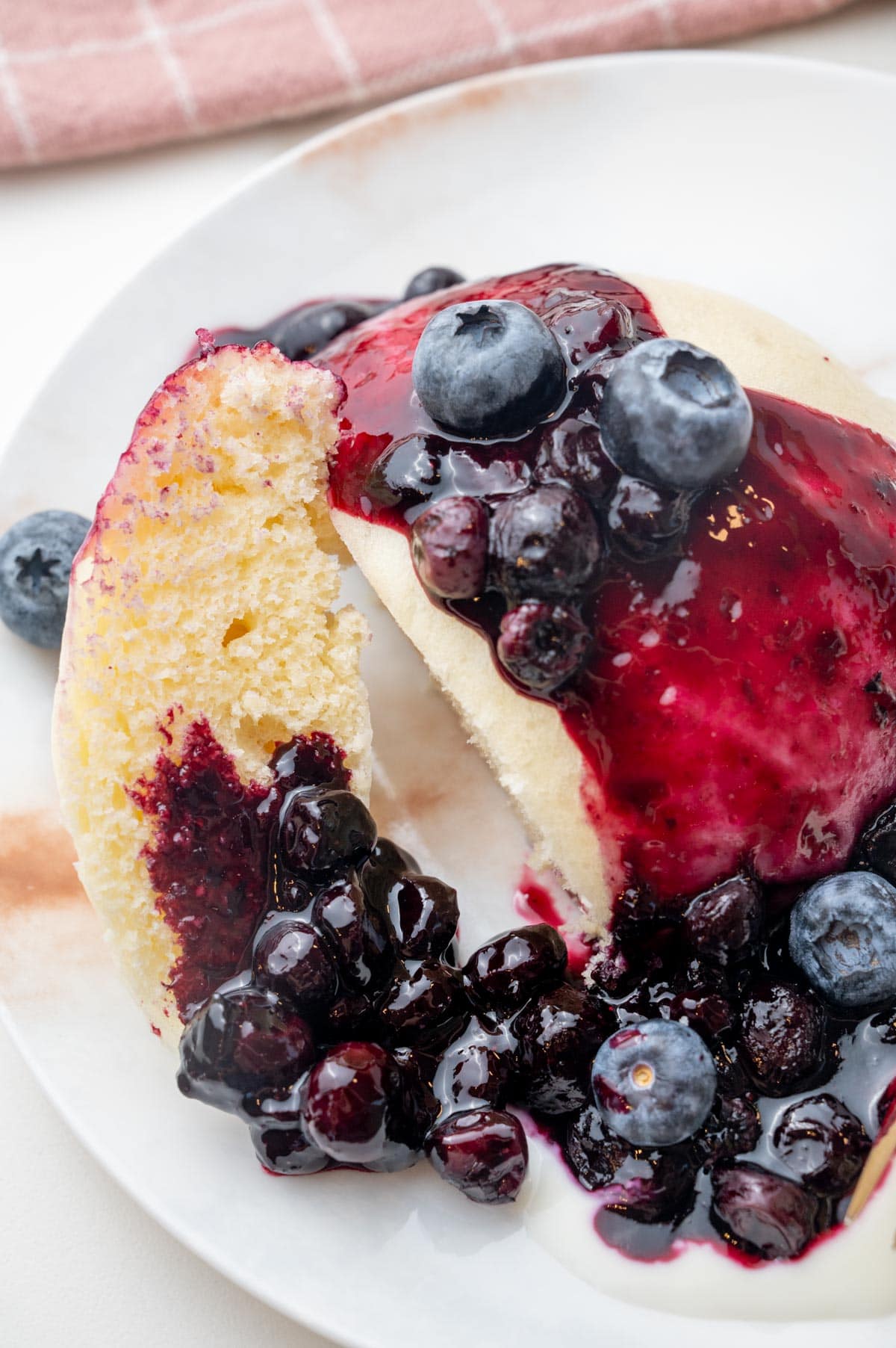 A close-up photo of steamed bun with blueberry sauce and yogurt on a white plate.