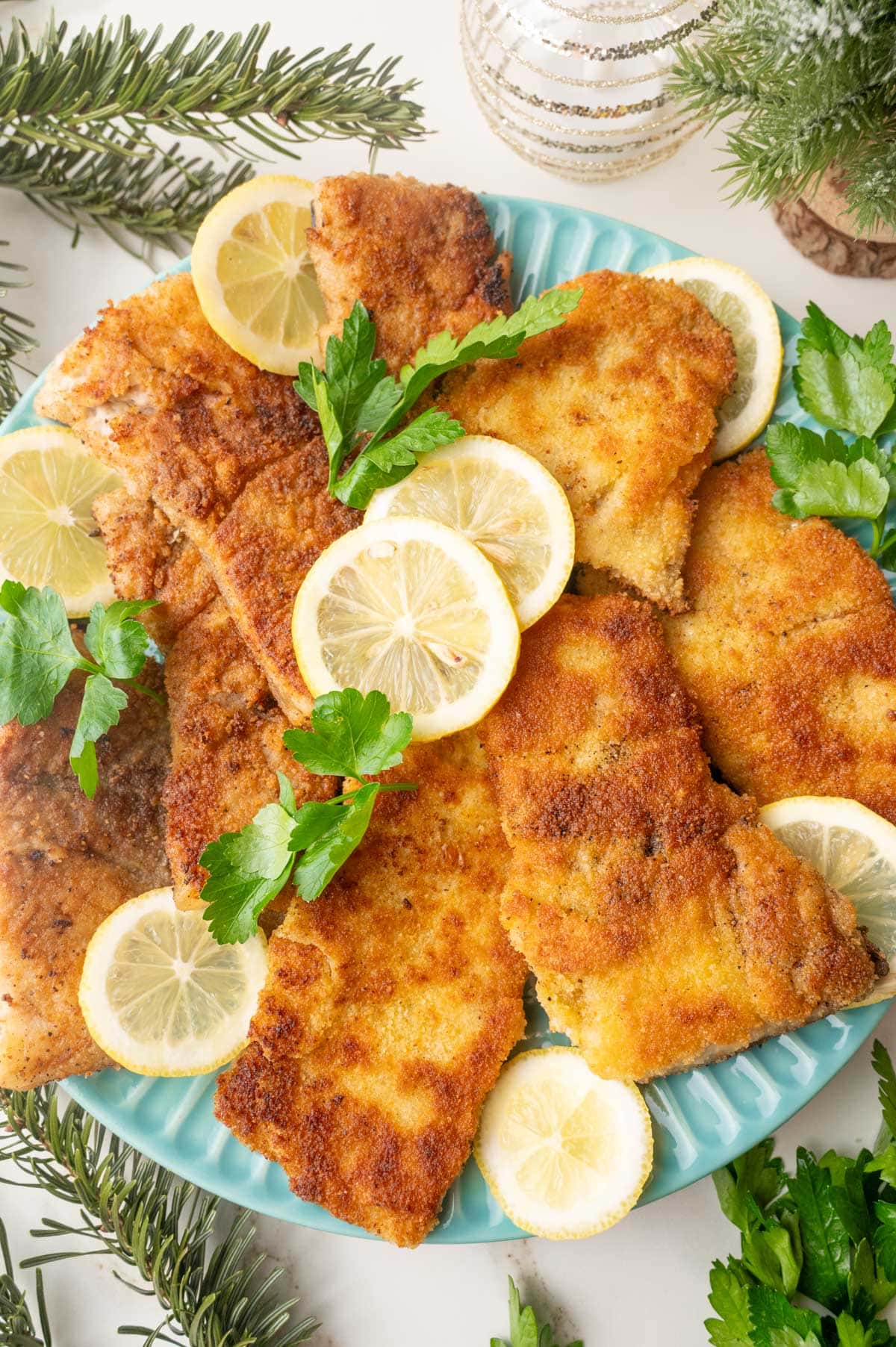 Pan-fried carp fillets on a blue plate with lemon slices and parsley leaves. Christmas decorations in the background.