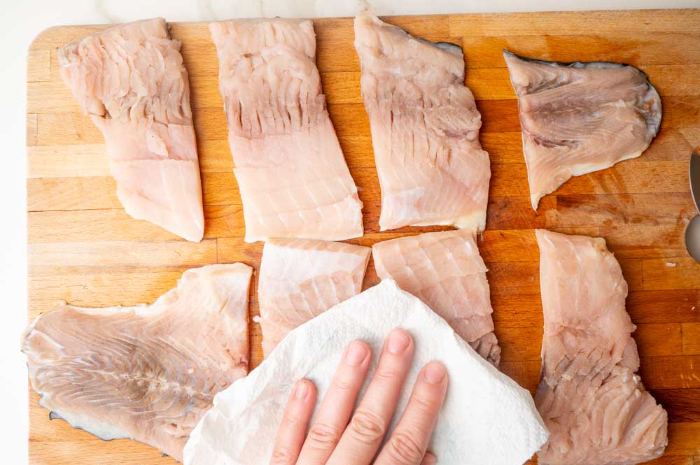 Carp fillets cut into smaller pieces are being dried with paper towels.