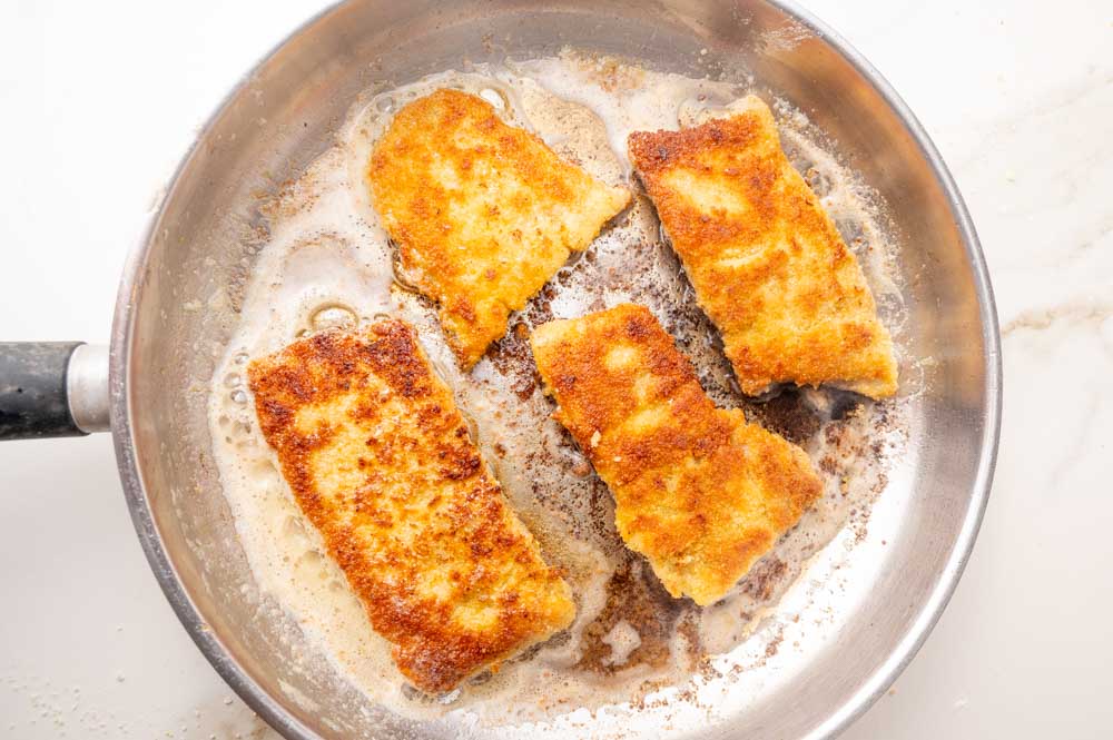 Breaded fish fillets are being fried in a pan.