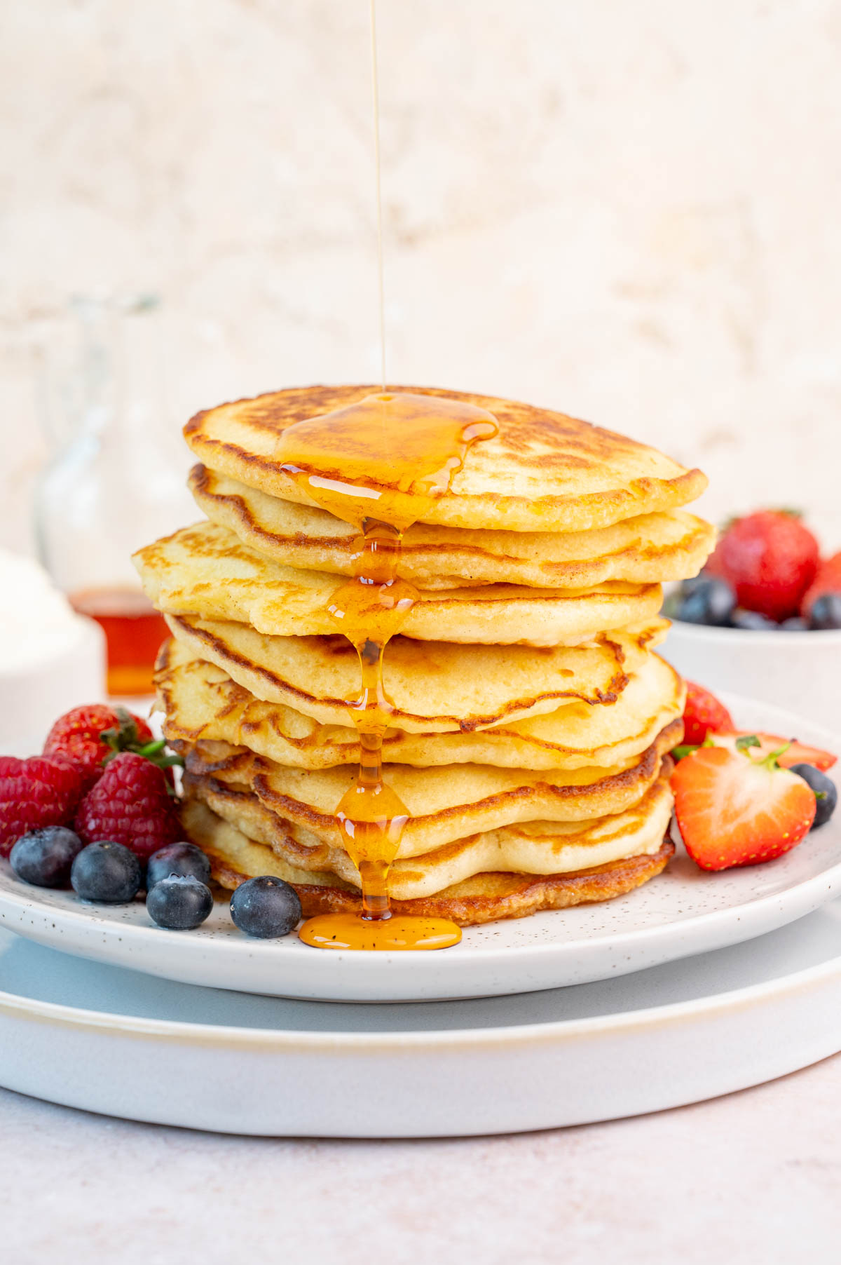 Maple syrup is being poured over a stack of pancakes.