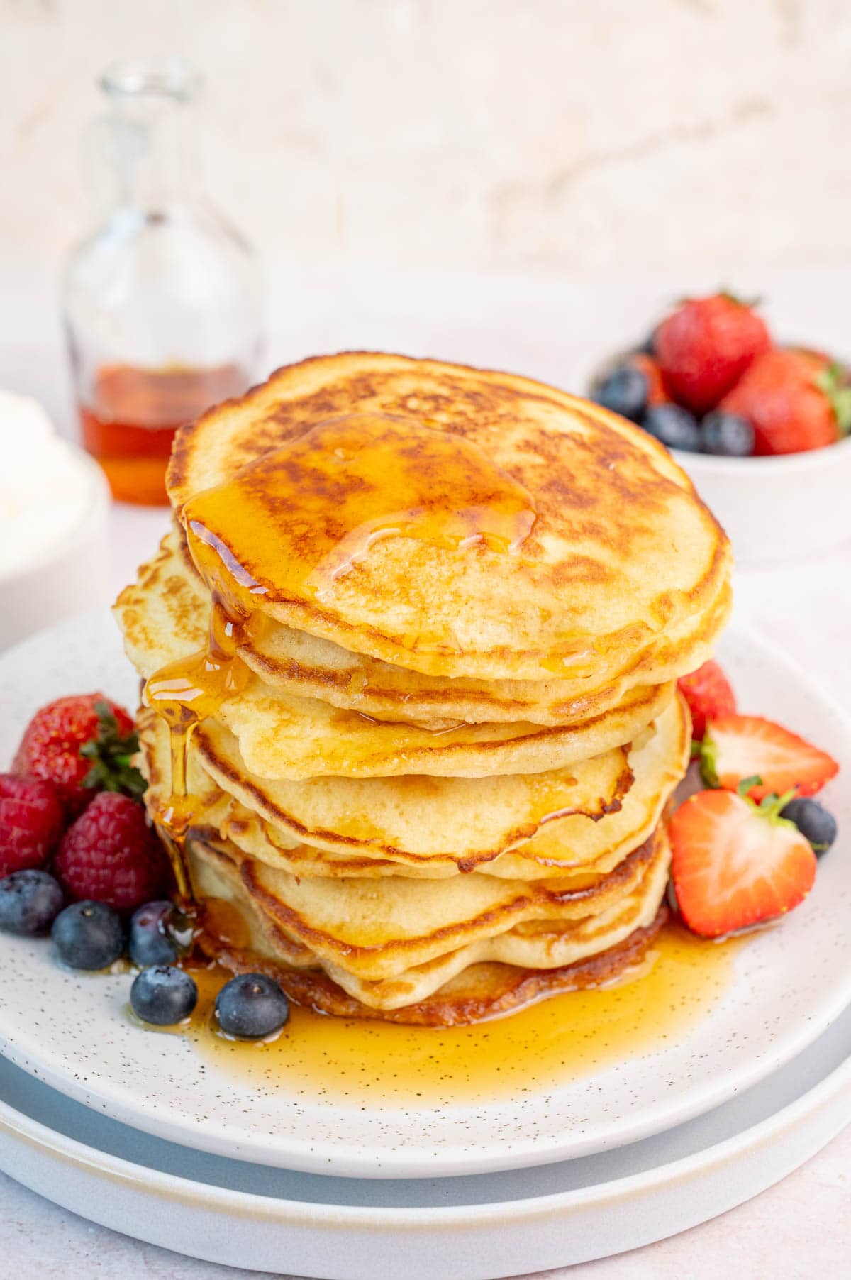 A stack of pancakes on a white plate with maple syrup and fresh berries.