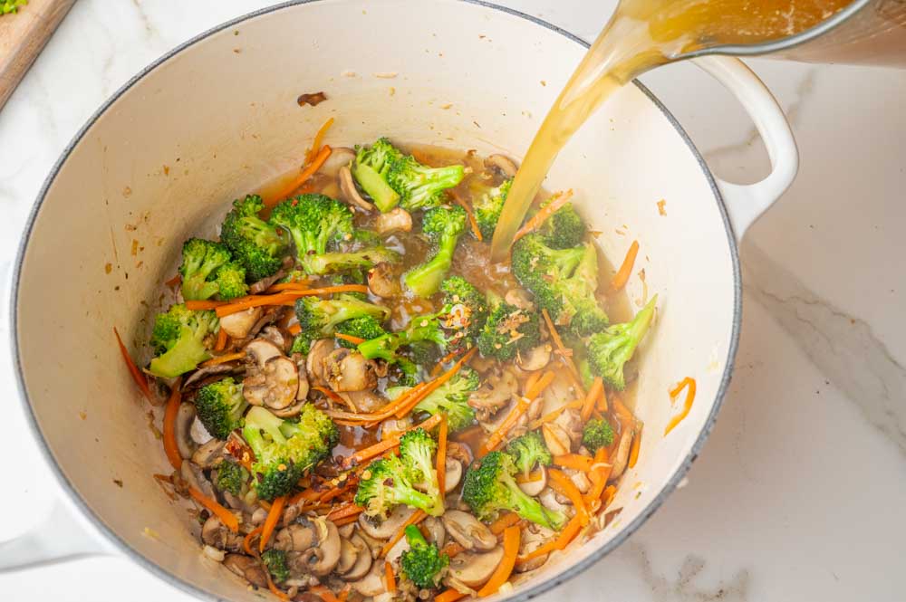 Broth is being added to sauteed vegetables in a pot.