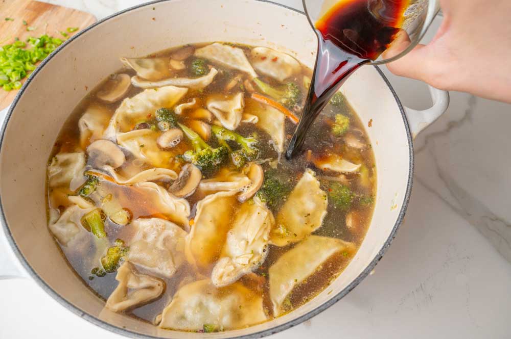 Potsticker soup is being seasoned with soy sauce.