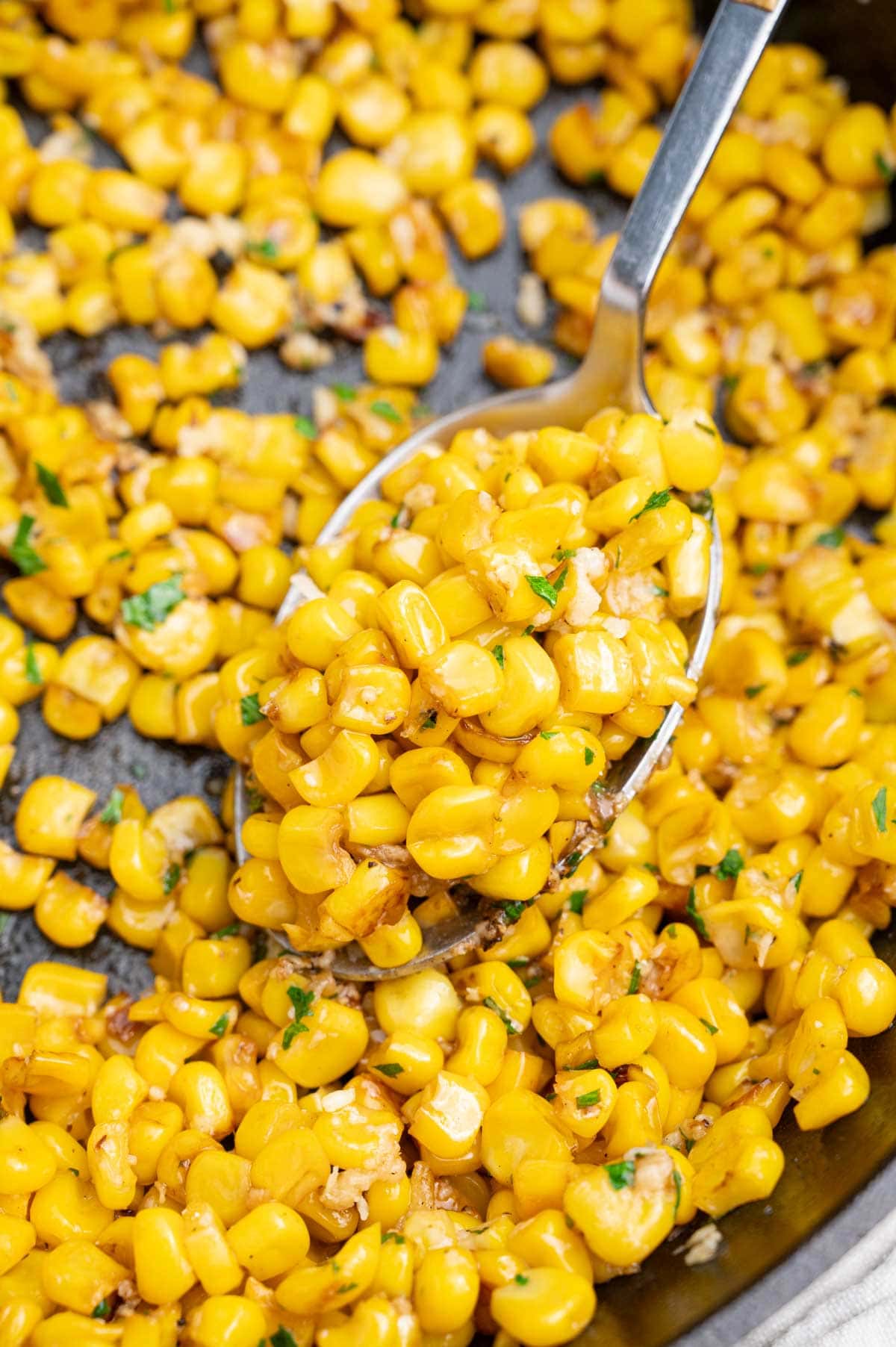 A close up photo of sautéed corn on a spoon in a black cast iron pan.