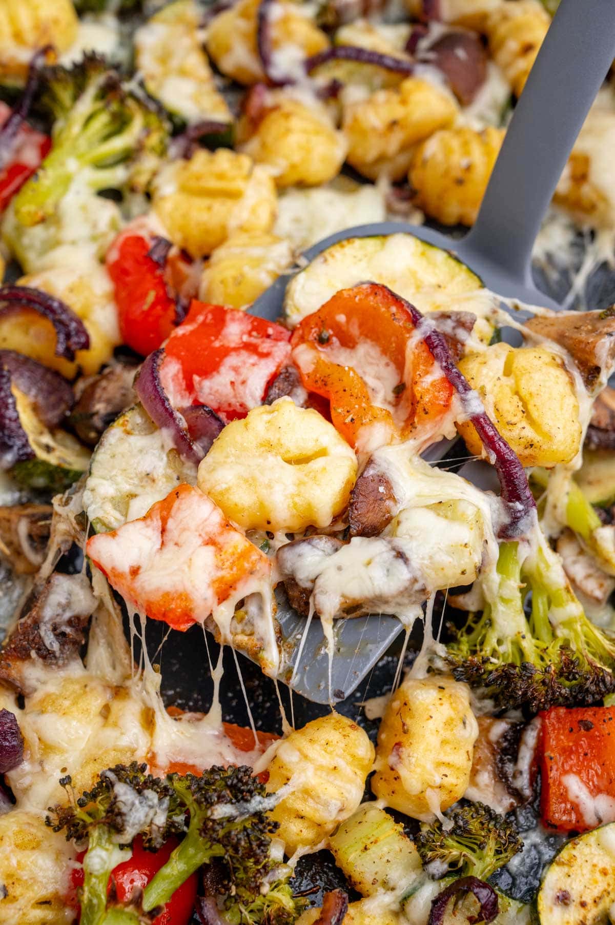 A close up photo of gnocchi with vegetables and cheese on a spatula.