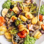 Baked gnocchi with vegetables and basil pesto on a beige plate.