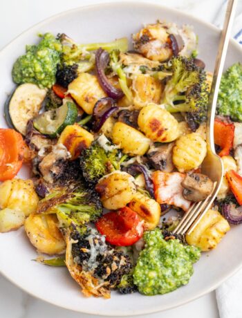 Baked gnocchi with vegetables and basil pesto on a beige plate.
