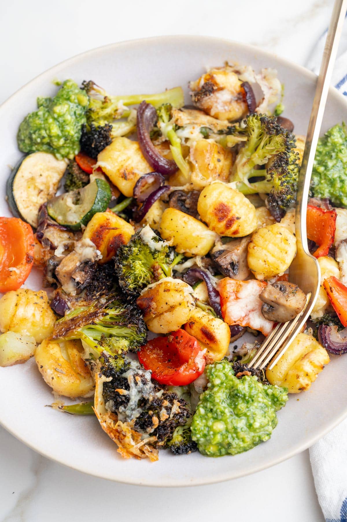 Sheet pan gnocchi and vegetables with basil pesto on a beige plate.