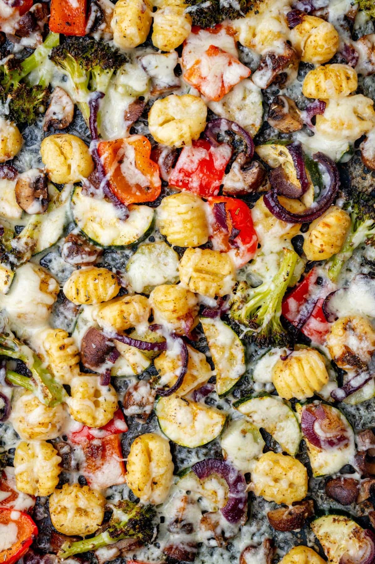 Baked gnocchi, vegetables and cheese on a black baking sheet.