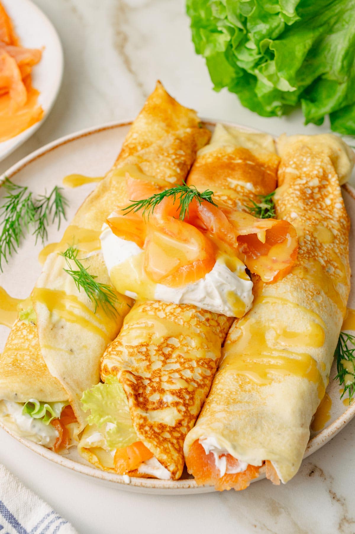 Savory crepes with smoked salmon, cream cheese and honey mustard sauce on a beige plate.