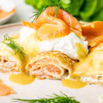 Smoked salmon crepes cut in half with honey mustard sauce on a beige plate.