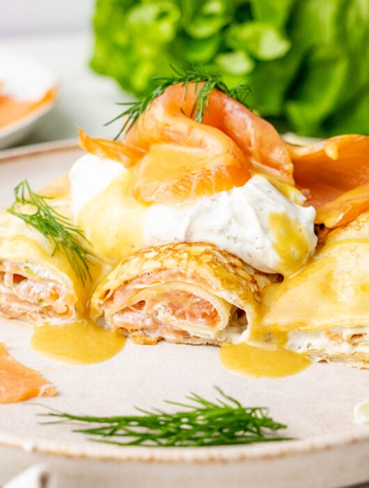 Smoked salmon crepes cut in half with honey mustard sauce on a beige plate.