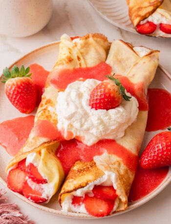 Crepes filled with whipped cream and fresh strawberries, served with strawberry sauce.