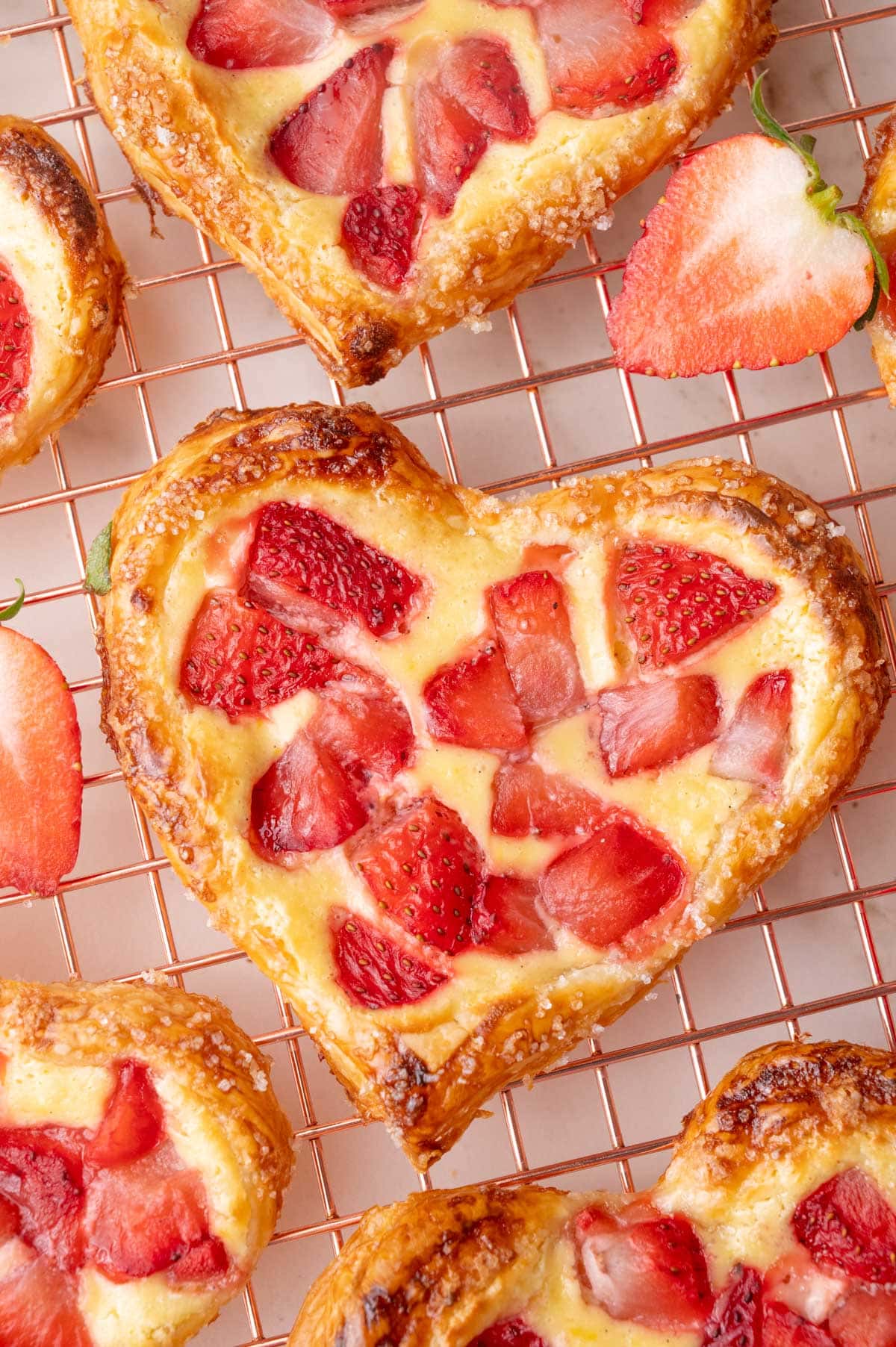 A close-up photo of Valentine's Strawberry Puff Pastry Hearts on a gold cooling rack.