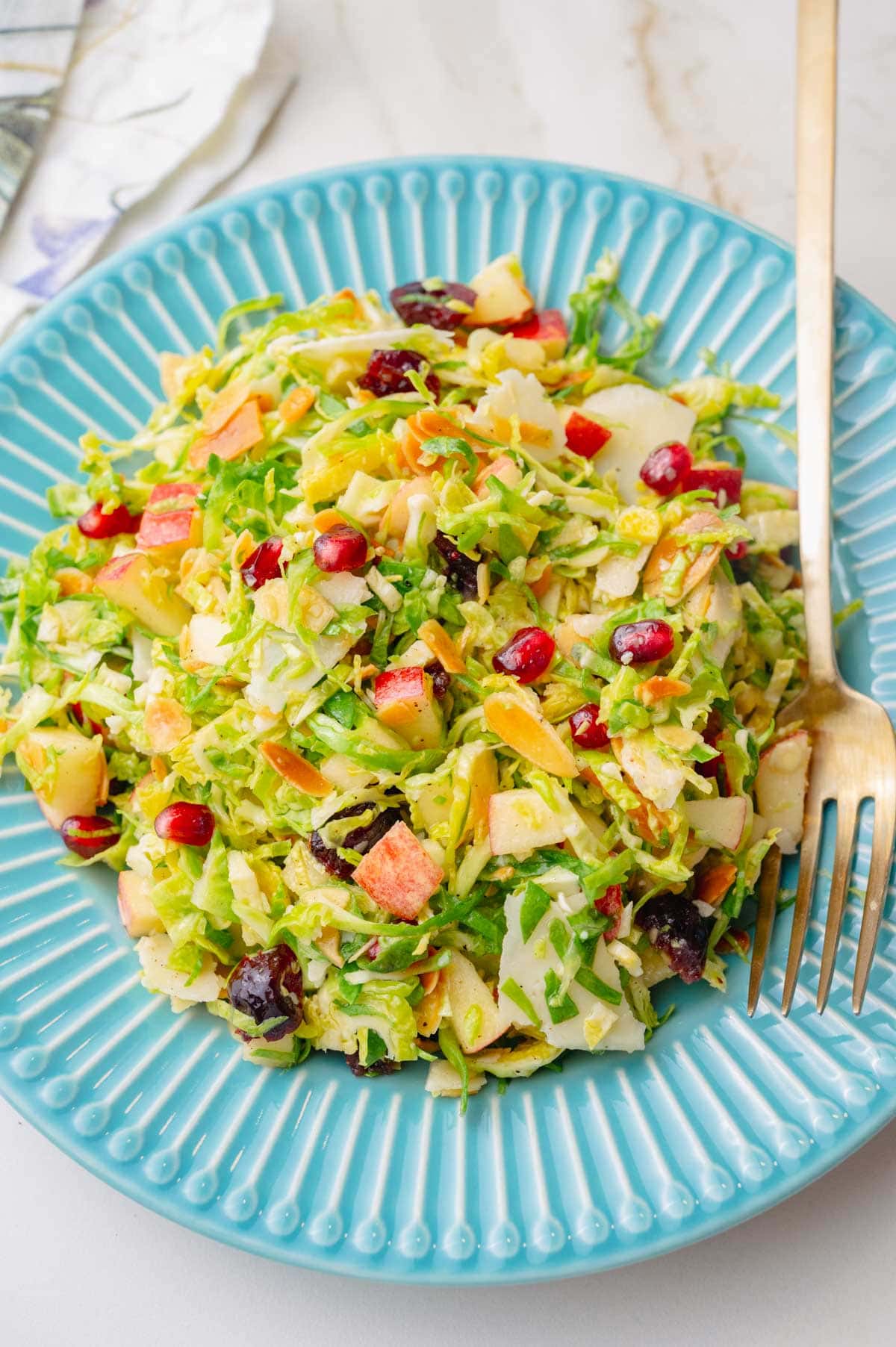 Shaved brussel sprouts salad on a blue plate with a gold fork on the side.