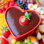 Chocolate fondue in a red heart-shaped fondue pot with a strawberry submerged in the chocolate.