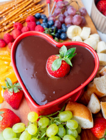 Chocolate fondue in a red heart-shaped fondue pot with a strawberry submerged in the chocolate.