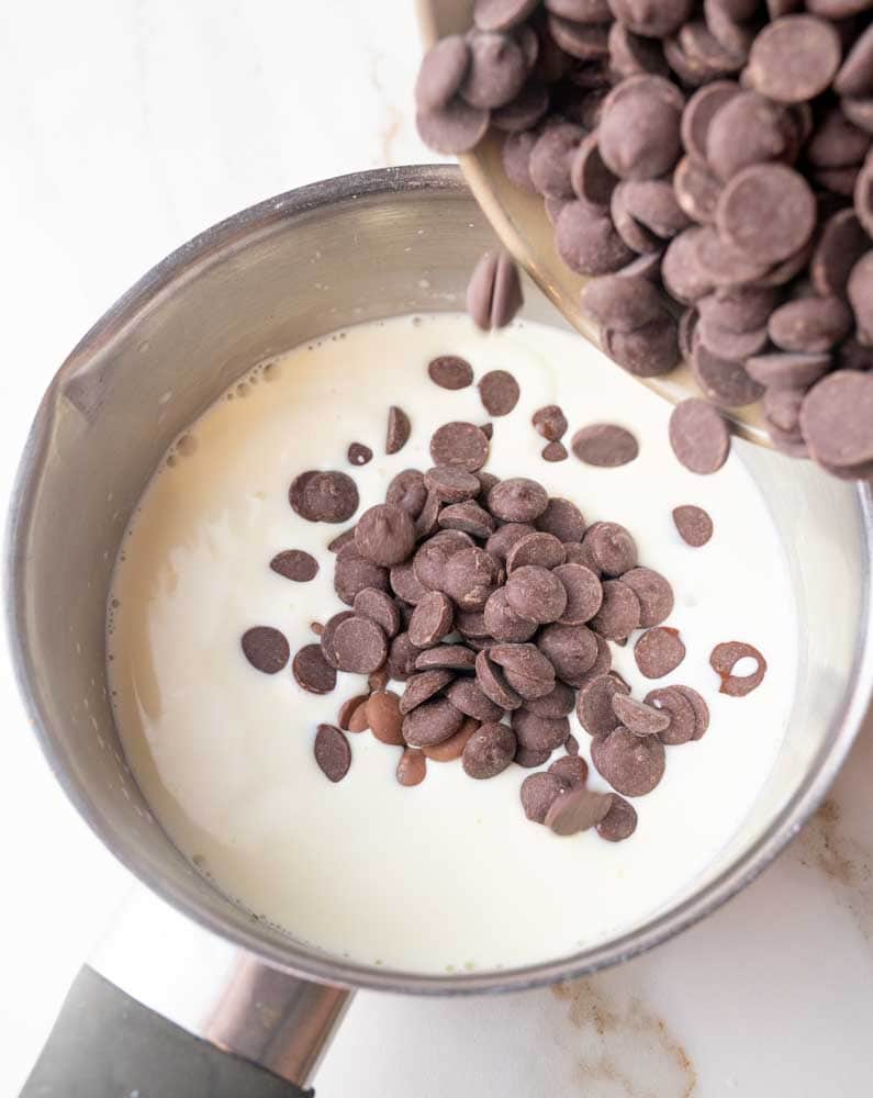 Chocolate chips are being added to a pot with cream and milk.