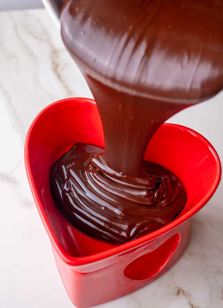 Chocolate sauce is being poured into chocolate fondue bowl.