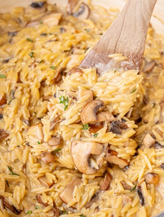 Mushroom orzo in a white pot with a wooden spatula.