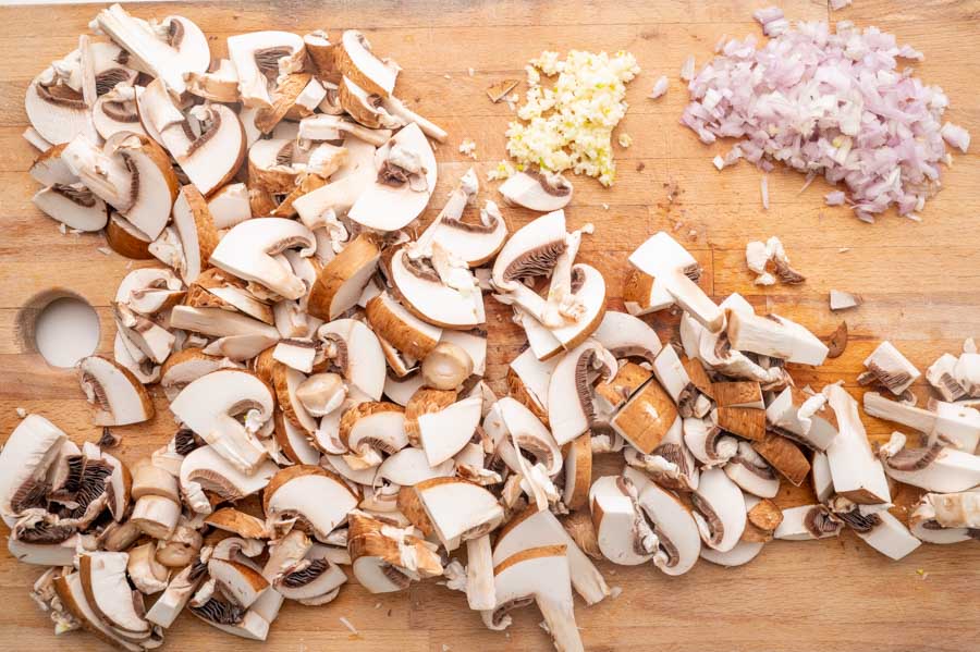 Chopped mushrooms, shallots, and garlic on a wooden board.
