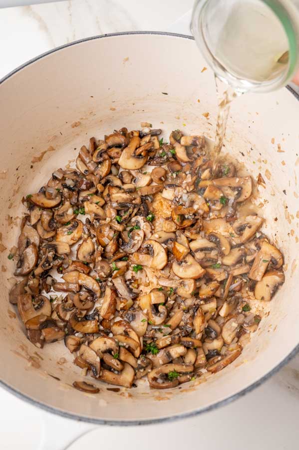 Wine is being added to a pot with sauteed mushrooms with onions and garlic.
