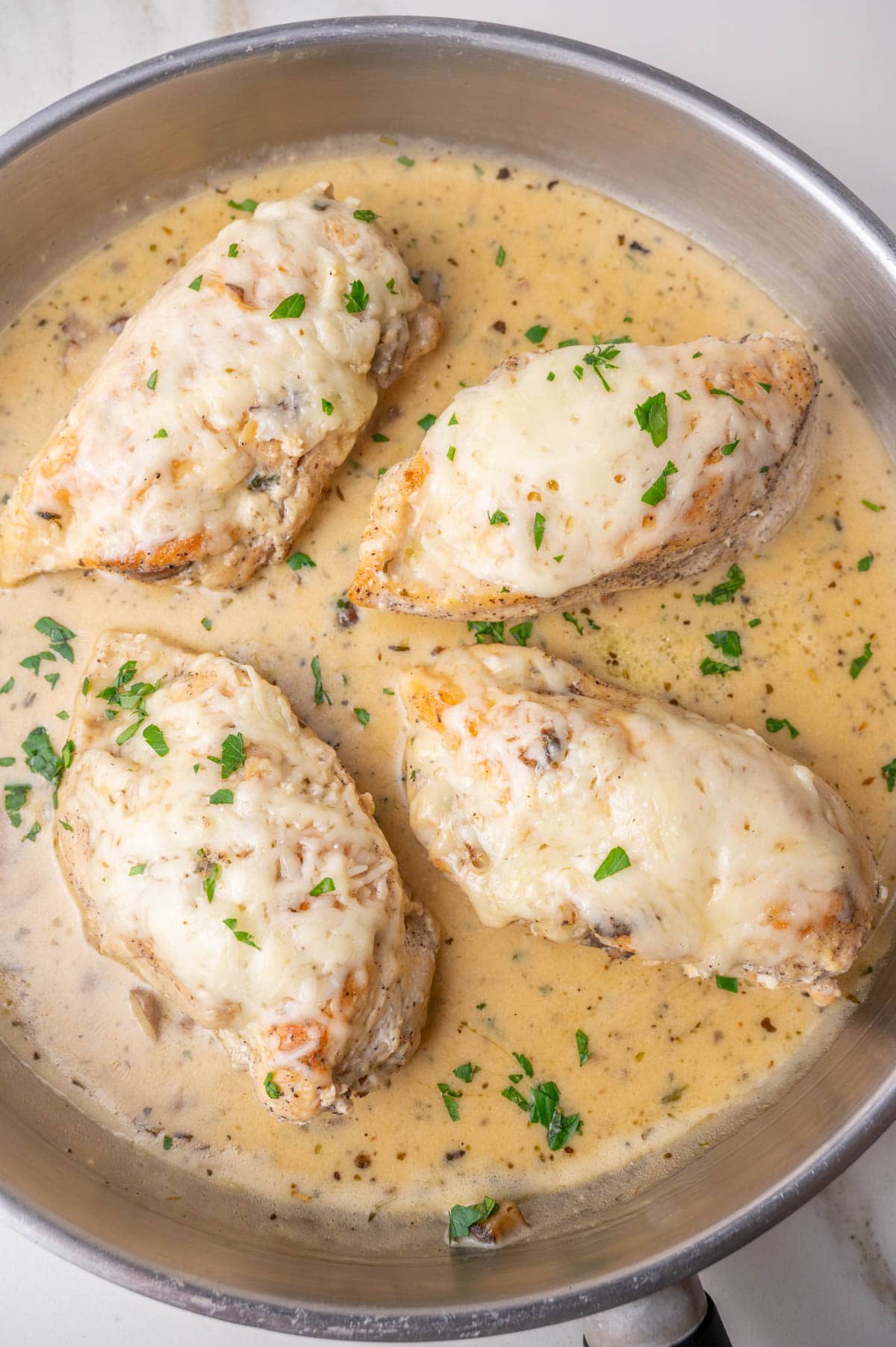 Four mushroom-stuffed chicken breasts in a creamy sauce in a pan.