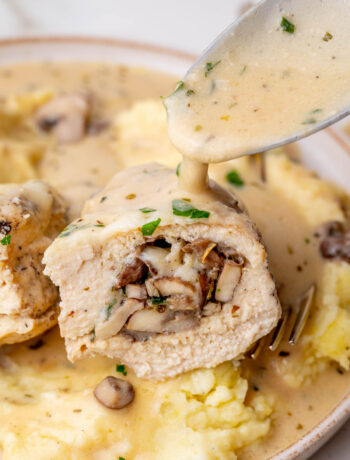 Cut in half mushroom-stuffed chicken breast is being poured with creamy sauce.