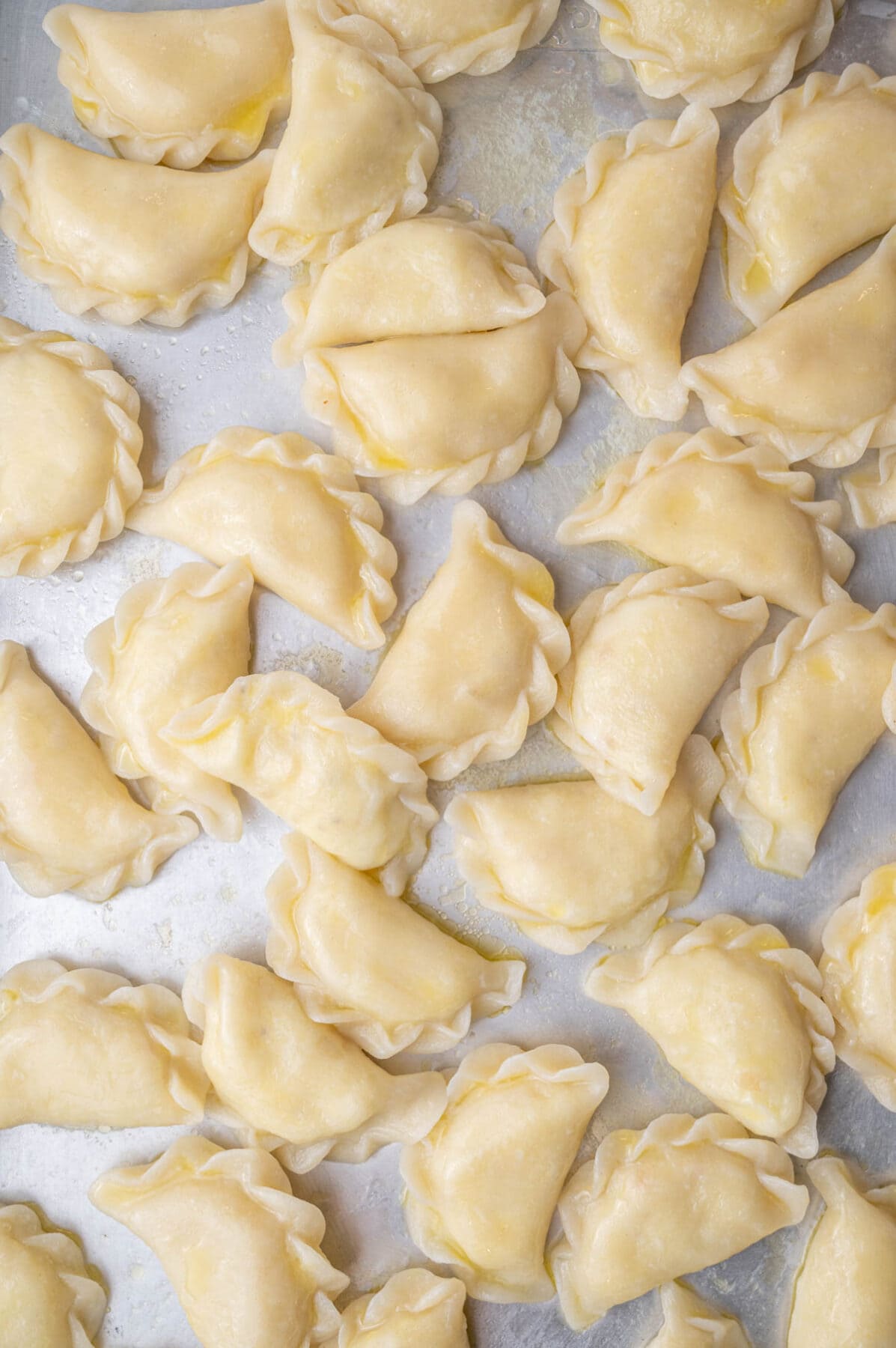 Freshly boiled pierogi ruskie topped with melted butter on a silver baking sheet.