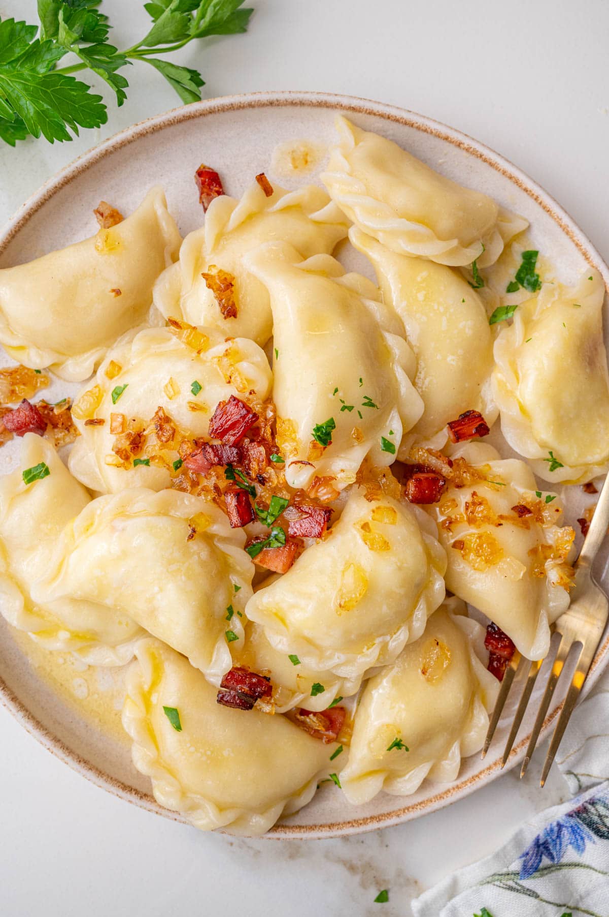 Potato and cheese pierogi topped with fried bacon and onions on a beige plate.