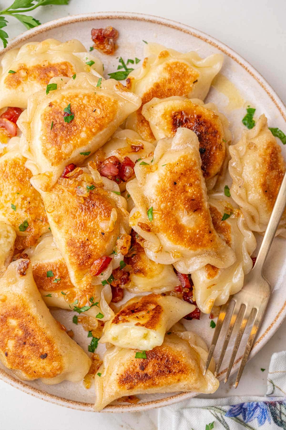 Pan fried potato and cheese pierogi with bacon and onion topping on a beige plate.