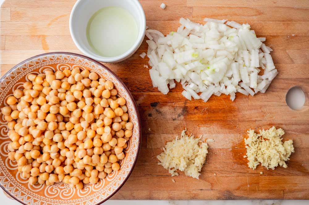 Chickpeas in a bowl. Chopped onion, grated garlic and ginger on a wooden board.