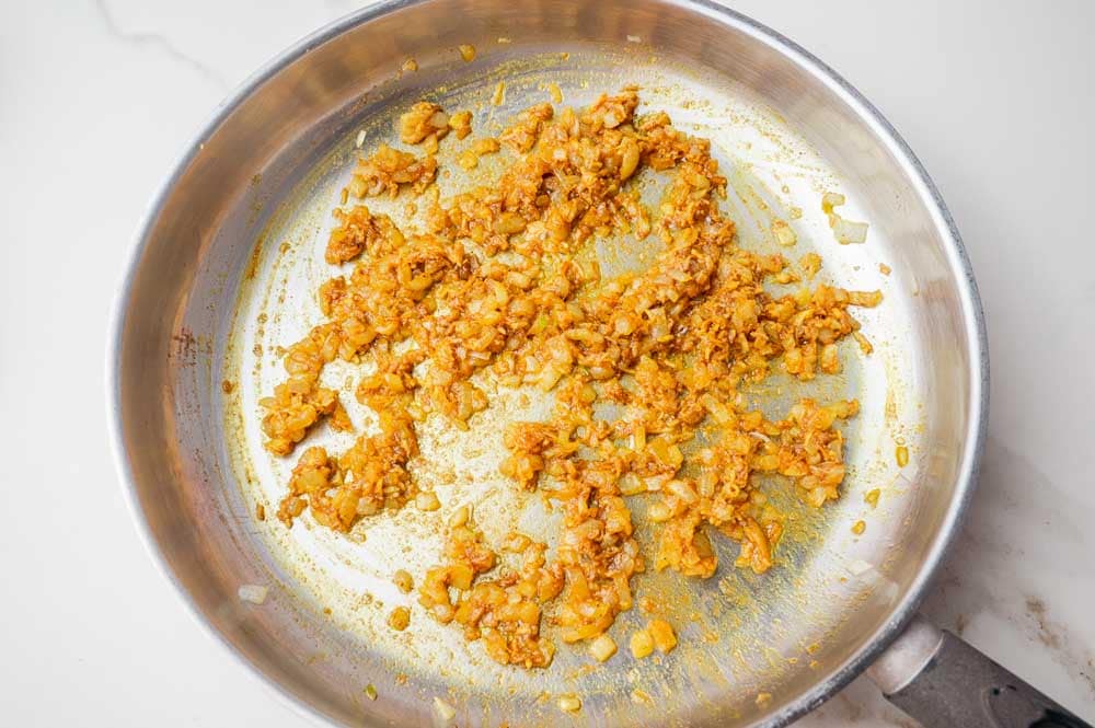 Sauteed onions with garlic, ginger, and spices in a pan.