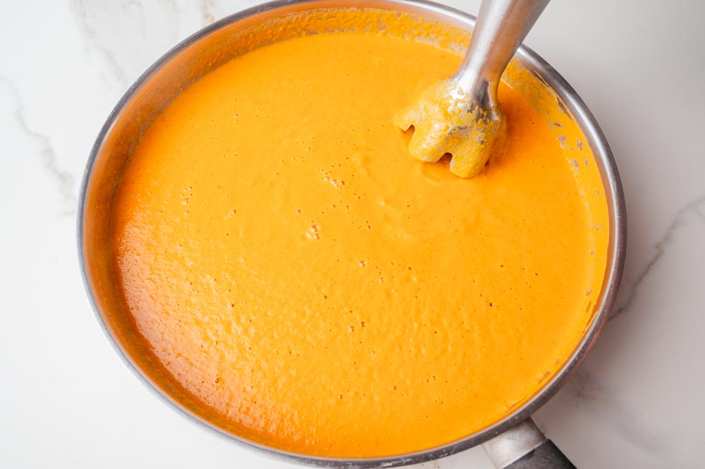 Curry sauce is being blended with immersion blended in a frying pan.