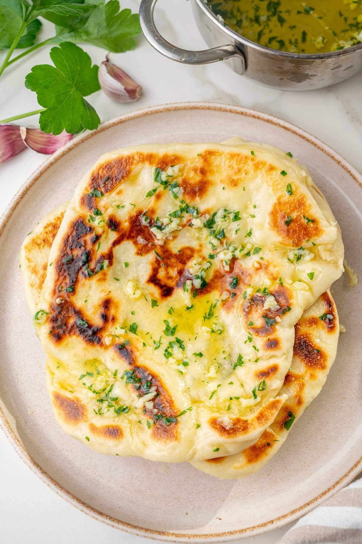 A stack of Naan bread with garlic butter on a beige plate.