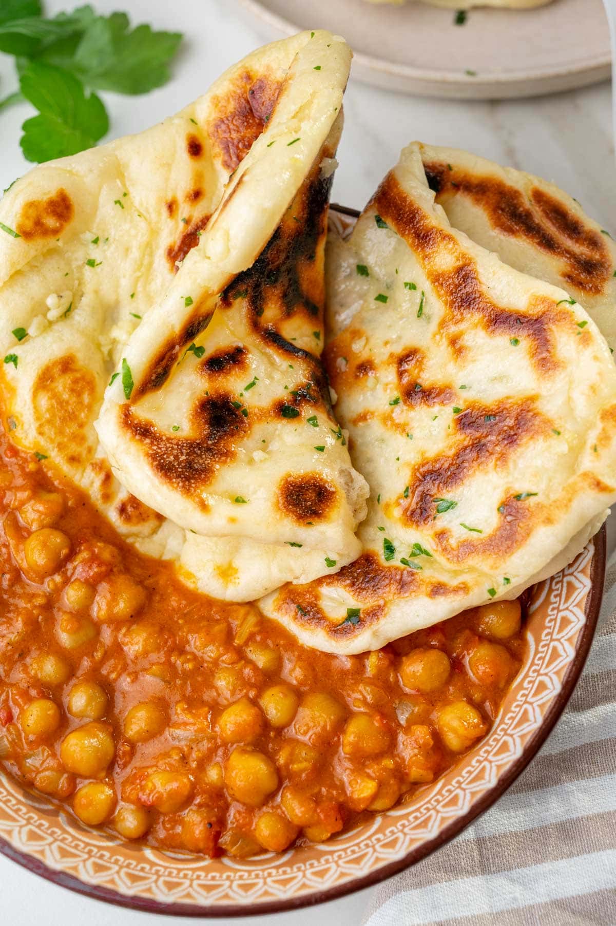 Chickpea curry in a bowl with Naan bread on top.