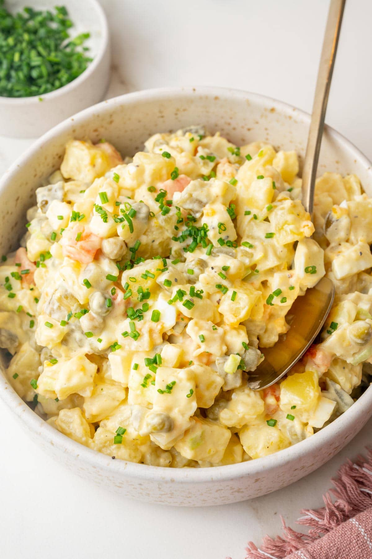 Polish salatka jarzynowa topped with chives in a beige bowl.