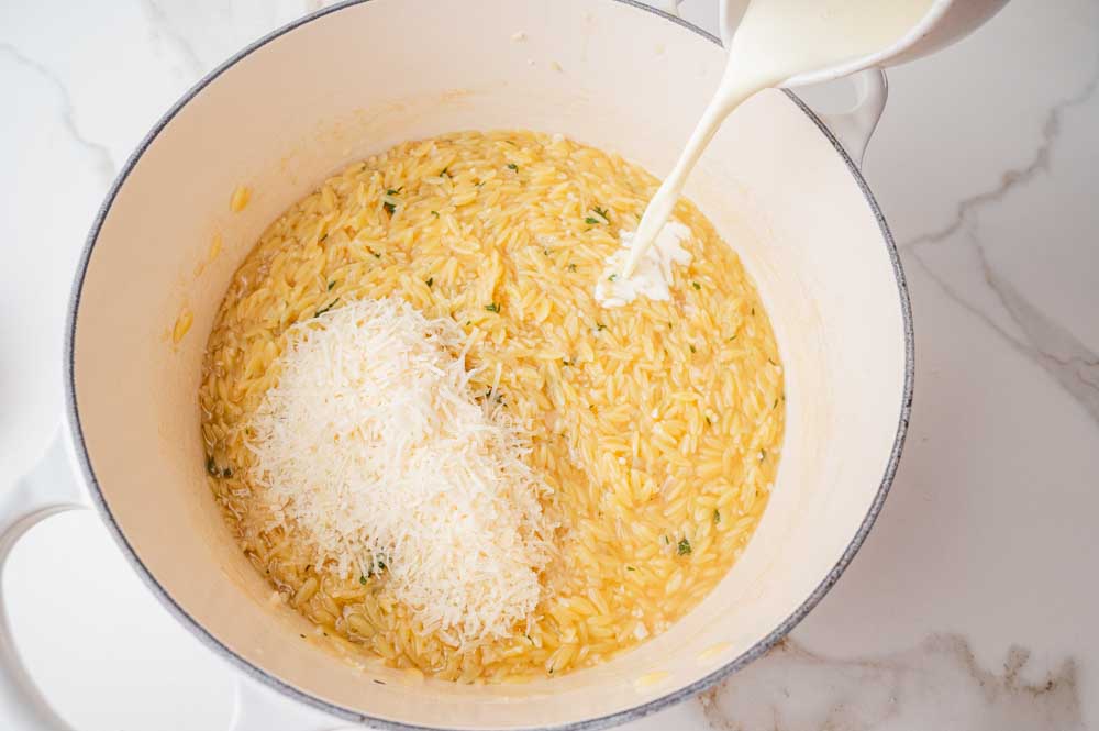 Heavy cream is being added to orzo and parmesan in a pot.