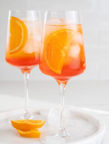 Two glasses with Aperol Spritz cocktail garnished with orange slices.