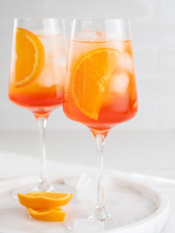 Two glasses with Aperol Spritz cocktail garnished with orange slices.