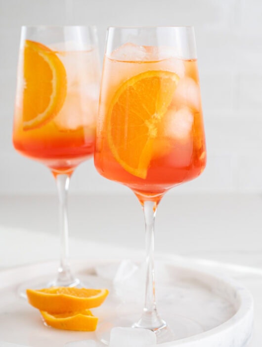 Two glasses with Aperol Spritz cocktail garnished with orange slices.