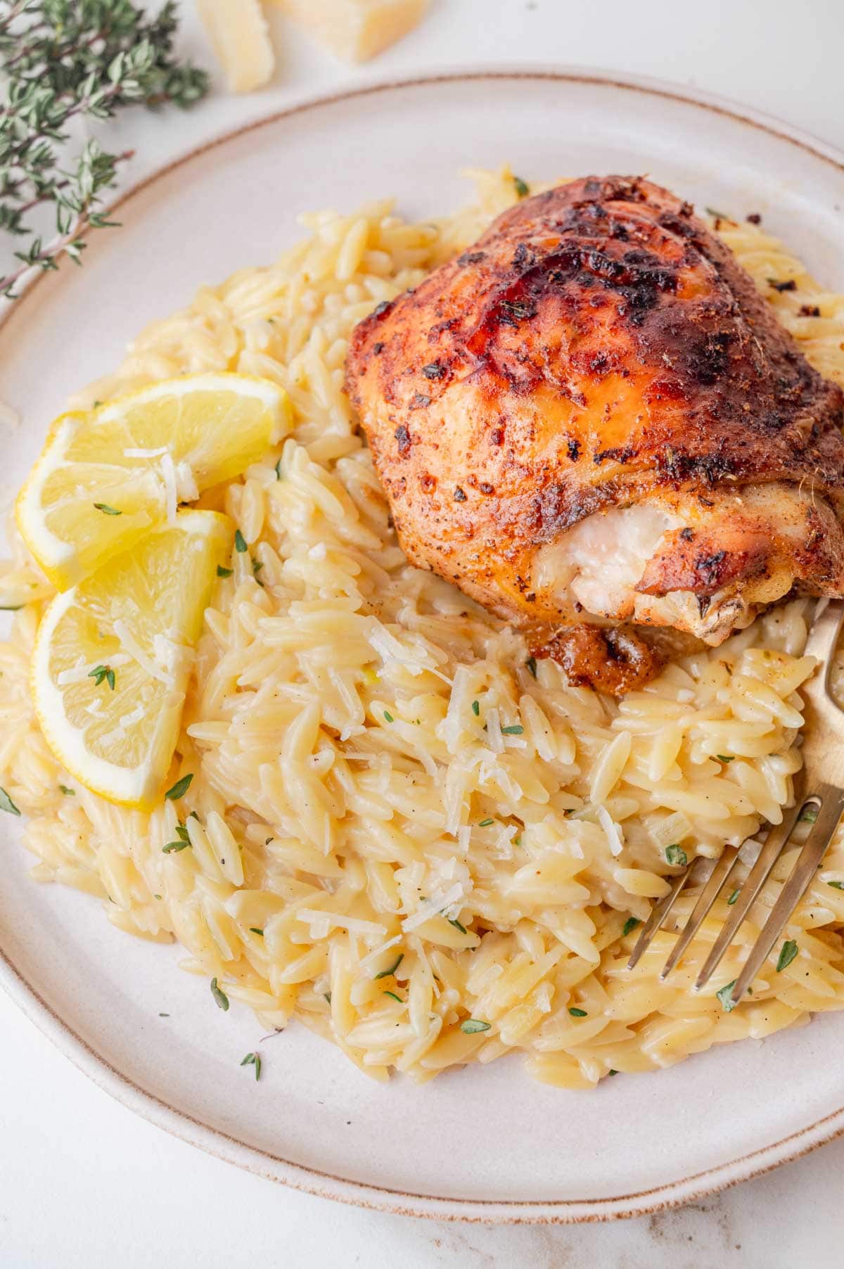 Lemon parmesan orzo on a plate topped with baked chicken thighs.