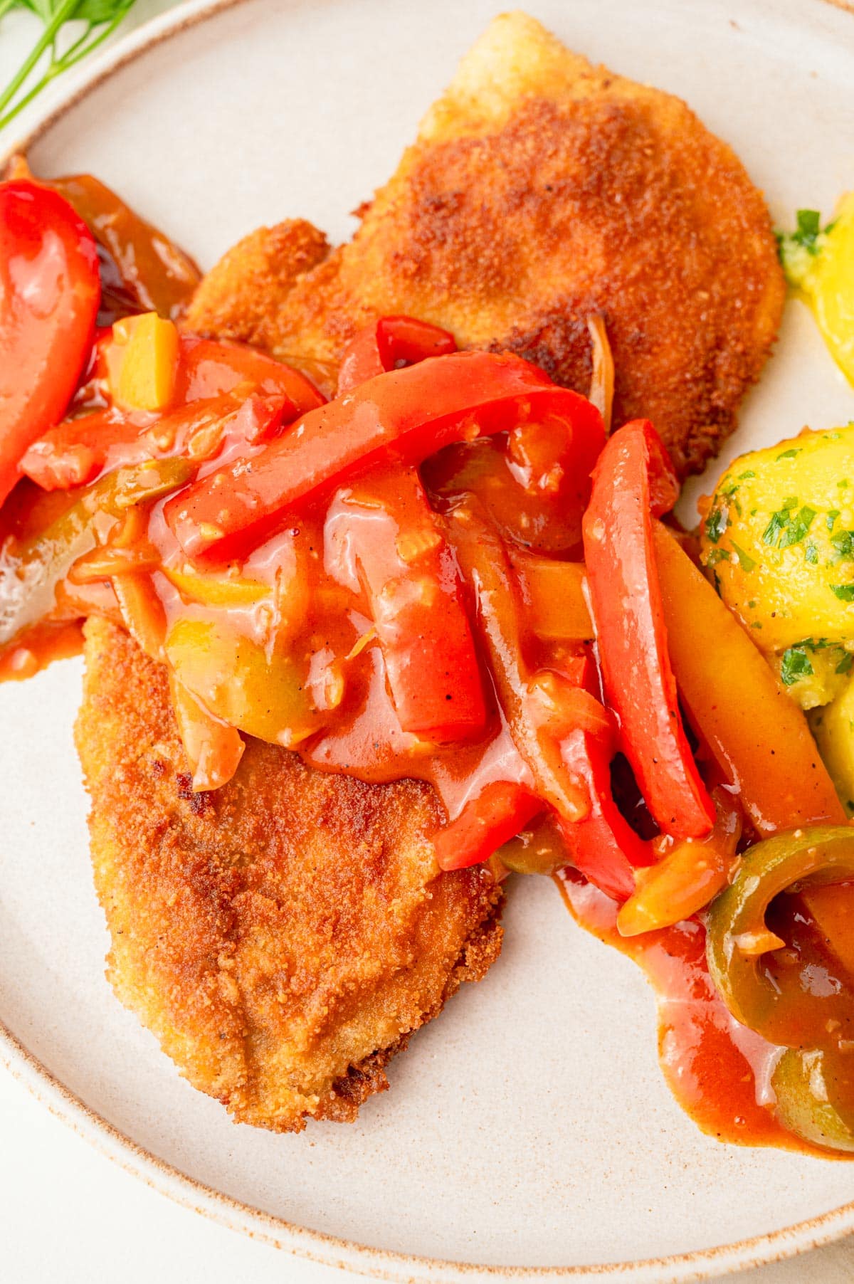 A close up photo of Zigeunerschnitzel with parsley potatoes on a beige plate.