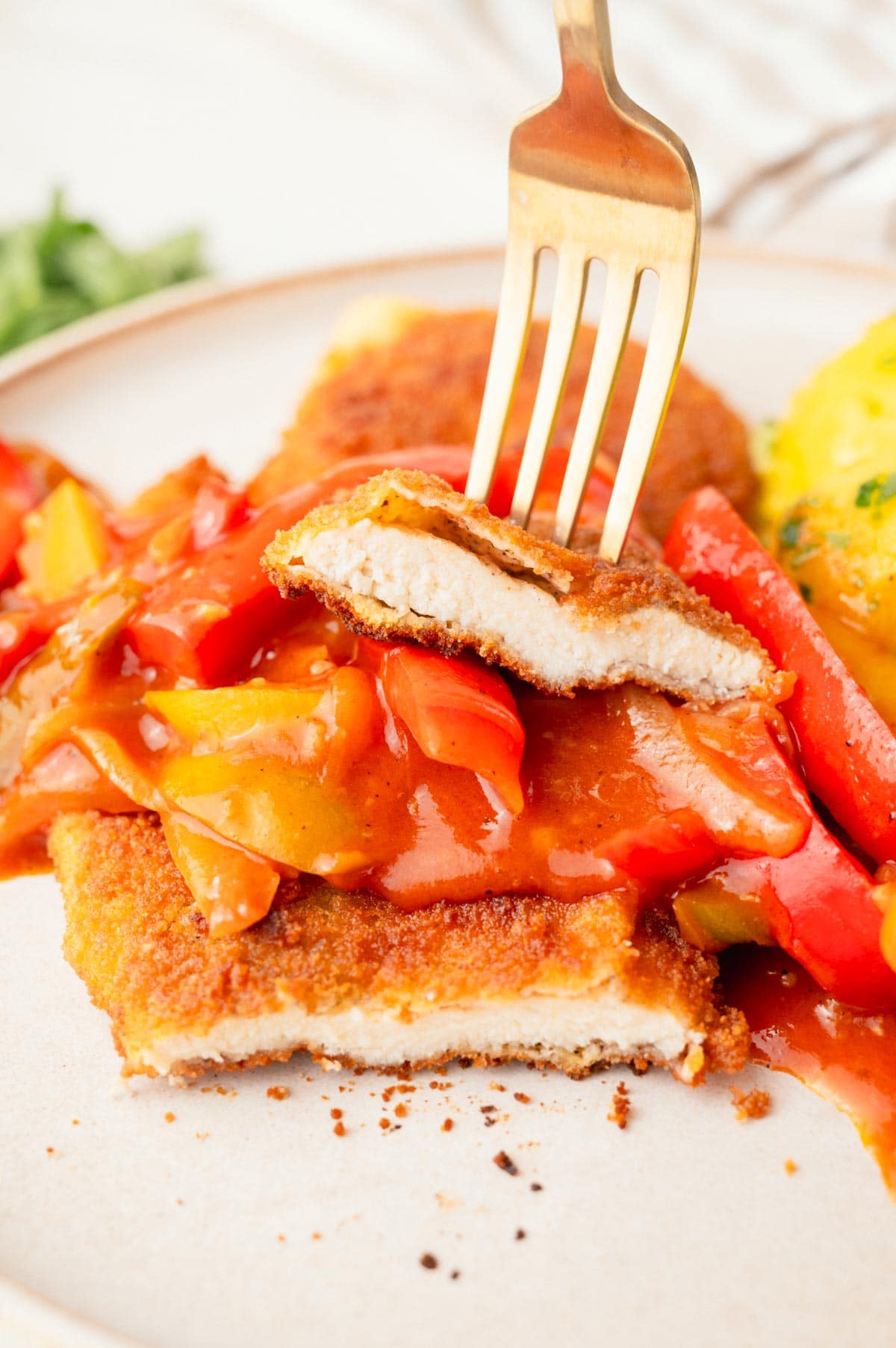 Chicken Schnitzel cut in half with bell pepper sauce on top on a plate.
