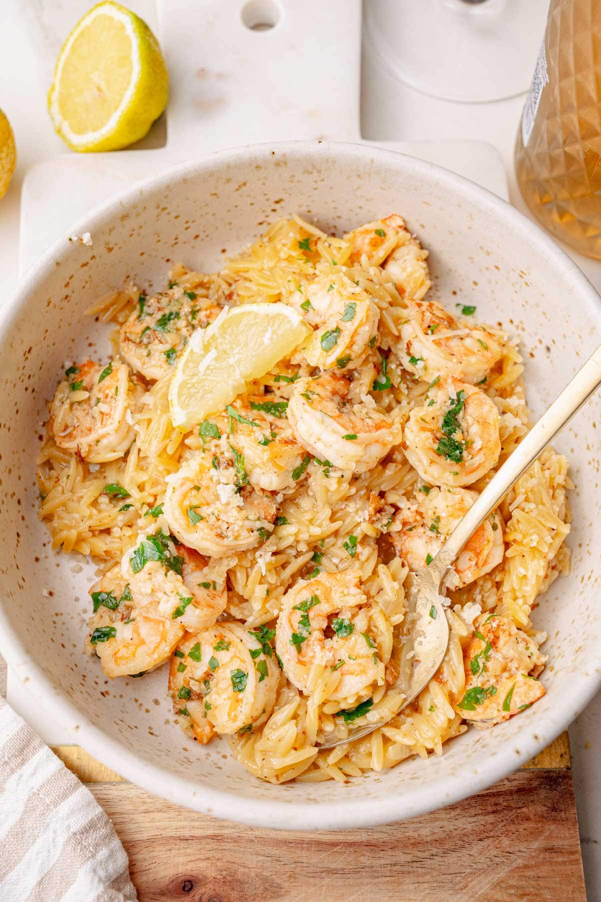 Makaron orzo z krewetkami w beżowym talerzu.