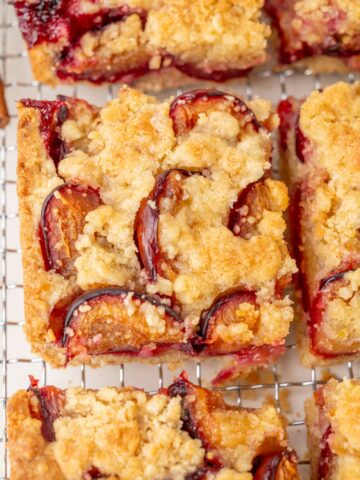 Close-up of a slice of German plum cake with a buttery crumb topping and baked plum halves, showing crisp edges and juicy fruit.